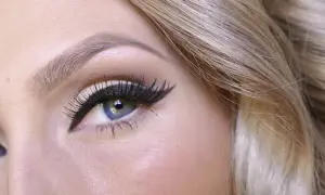 En närbild på ett blått öga med perfekt målad eyeliner och långa fransar. Håret är blont och böljande.