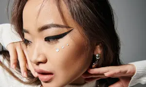 En närbild på en ung kvinna med en dramatisk eyeliner vinge, glittrande kristaller på kinden och en silverfärgad örhänge.
