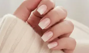 En hand med snygga naglar ombre i en mjuk, ljus ton. Naglarna har en gradvis övergång från en ljusrosa bas till vita toppar, vilket ger en elegant och naturlig look.