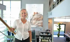 En kvinna ler vid en trappa. Bakom henne syns en stor bild med texten "MARIA ÅKERBERG".