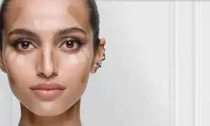 En kvinna förbereder sig för att applicera concealer. Hon har ljusa och mörka nyanser av smink på kinderna, näsan och pannan för att forma ansiktet.