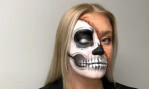 En kvinna med en otrolig ansiktsmålning för halloween. Halva ansiktet är målat som ett skelett med en vit pupill, medan andra halvan visar en realistisk, trasig hudeffekt.
