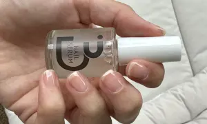 En hand håller en flaska nagelserum. Naglarna är naturliga och visar tecken på att de skivar sig, men serumet kan hjälpa till att stärka dem.
