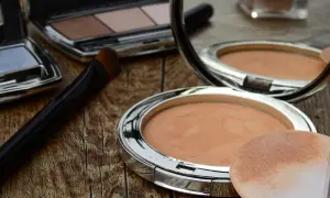 Sminka rynkor med puder och borste. En spegel reflekterar sminkprodukter på en träyta.