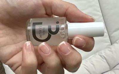 En hand håller en flaska nagelserum. Naglarna är naturliga och visar tecken på att de skivar sig, men serumet kan hjälpa till att stärka dem.
