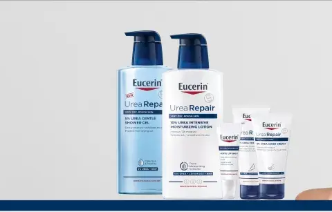 En kvinna ler med en Eucerin UreaRepair-produkt i bakgrunden. Serien innehåller karbamid för ansikte och kropp.