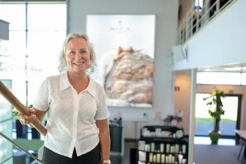 En kvinna ler vid en trappa. Bakom henne syns en stor bild med texten "MARIA ÅKERBERG".
