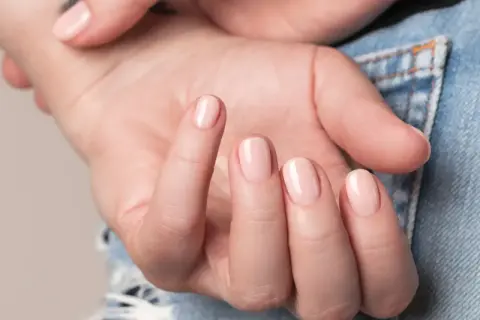 Nära bild på en hand med ljusrosa, glansiga naglar som ser ut som lipgloss nails.