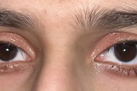 Närbild på ögon med glittrig douyin makeup i rosa toner. Ögonbrynen är mörka och buskiga.