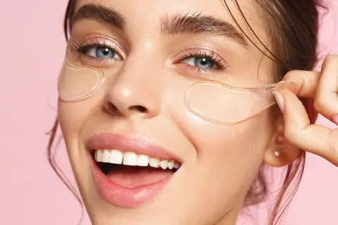 En kvinna ler glatt med eye patches under ögonen. Se hur eye patches sitta för bästa resultat.