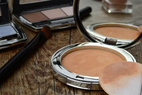 Sminka rynkor med puder och borste. En spegel reflekterar sminkprodukter på en träyta.