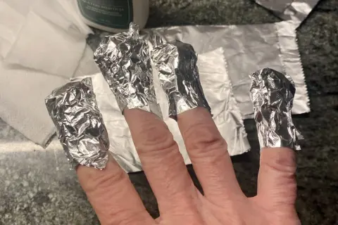 Fingrar inslagna i folie för att ta bort gellack hemma.
