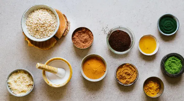 Ingredienser för hemmagjord peeling socker: havregryn, kakaopulver, kaffesump, gurkmeja, matcha och olja.