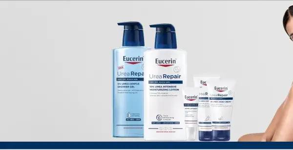 En kvinna ler med en Eucerin UreaRepair-produkt i bakgrunden. Serien innehåller karbamid för ansikte och kropp.
