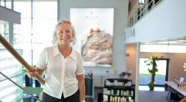 En kvinna ler vid en trappa. Bakom henne syns en stor bild med texten "MARIA ÅKERBERG".