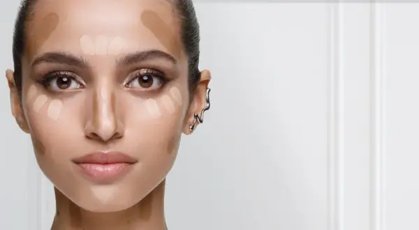 En kvinna förbereder sig för att applicera concealer. Hon har ljusa och mörka nyanser av smink på kinderna, näsan och pannan för att forma ansiktet.