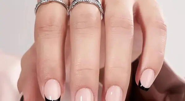 Ett par händer med eleganta press on nails i fransk manikyr med svarta toppar. Två glittrande ringar pryder fingrarna.
