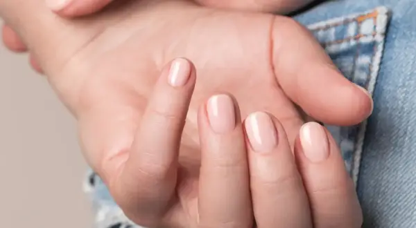 Nära bild på en hand med ljusrosa, glansiga naglar som ser ut som lipgloss nails.