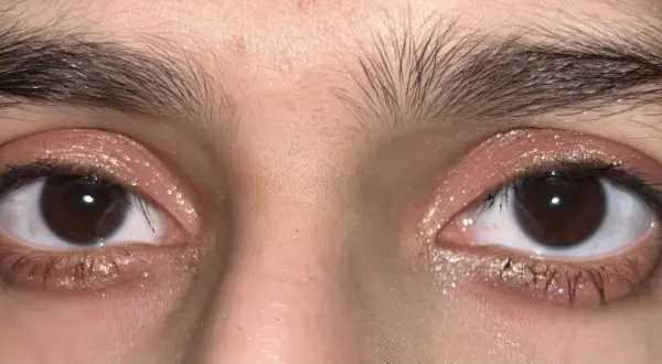 Närbild på ögon med glittrig douyin makeup i rosa toner. Ögonbrynen är mörka och buskiga.