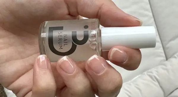 En hand håller en flaska nagelserum. Naglarna är naturliga och visar tecken på att de skivar sig, men serumet kan hjälpa till att stärka dem.