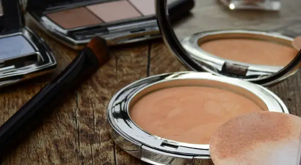 Sminka rynkor med puder och borste. En spegel reflekterar sminkprodukter på en träyta.