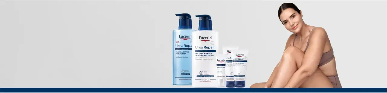 En kvinna ler med en Eucerin UreaRepair-produkt i bakgrunden. Serien innehåller karbamid för ansikte och kropp.