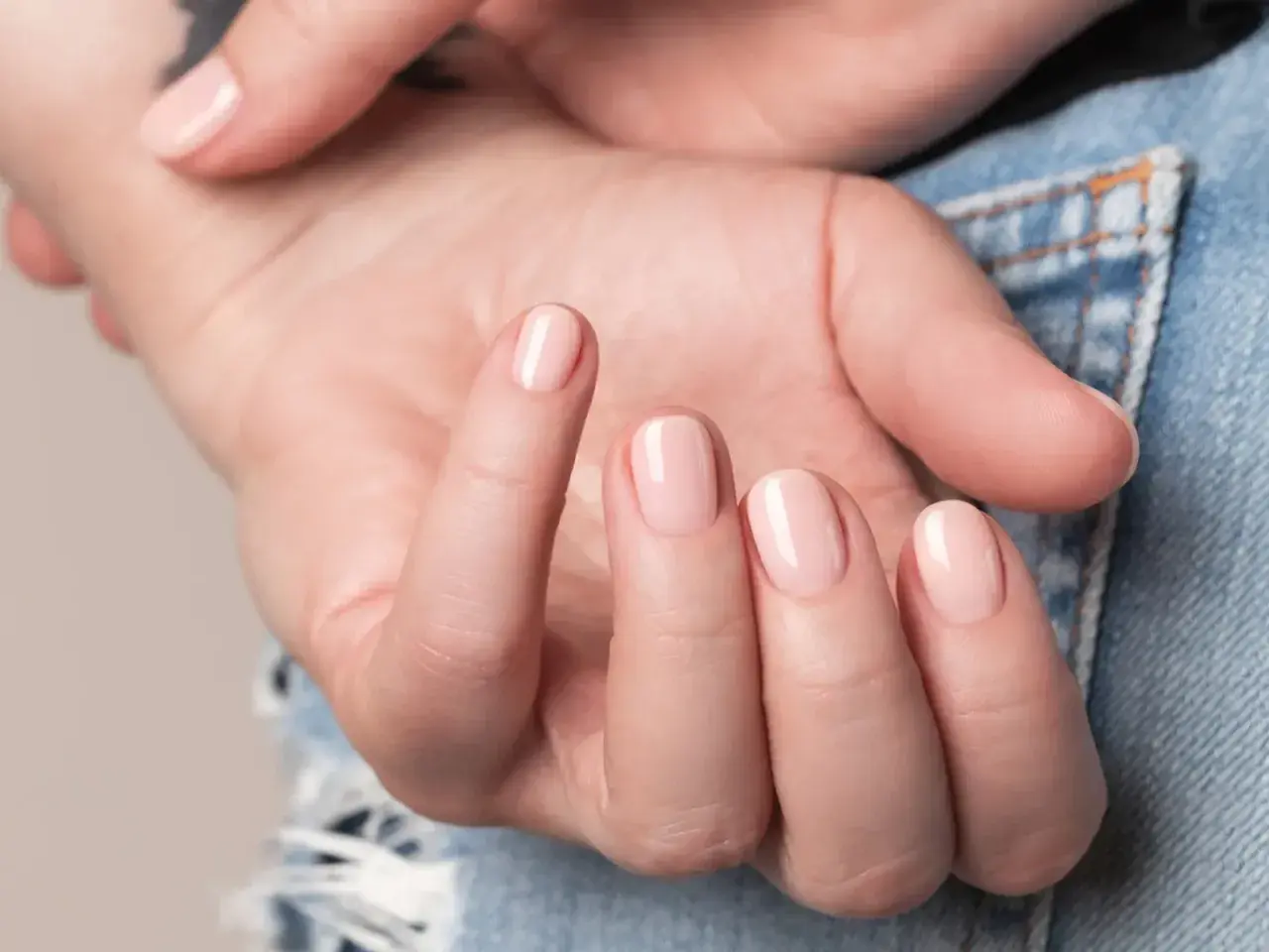 Nära bild på en hand med ljusrosa, glansiga naglar som ser ut som lipgloss nails.