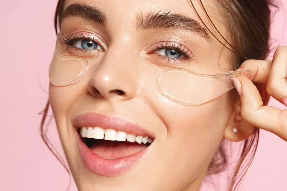 En kvinna ler glatt med eye patches under ögonen. Se hur eye patches sitta för bästa resultat.