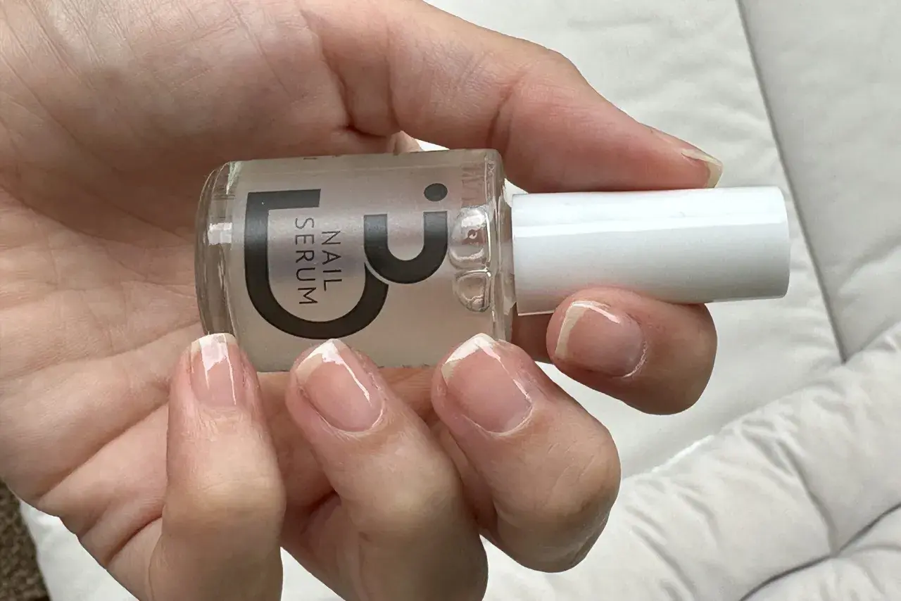 En hand håller en flaska nagelserum. Naglarna är naturliga och visar tecken på att de skivar sig, men serumet kan hjälpa till att stärka dem.