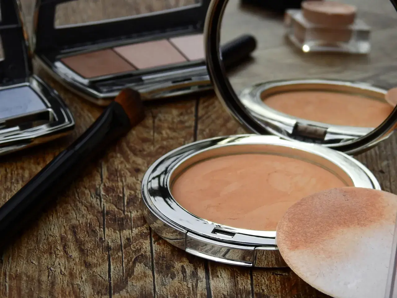 Sminka rynkor med puder och borste. En spegel reflekterar sminkprodukter på en träyta.
