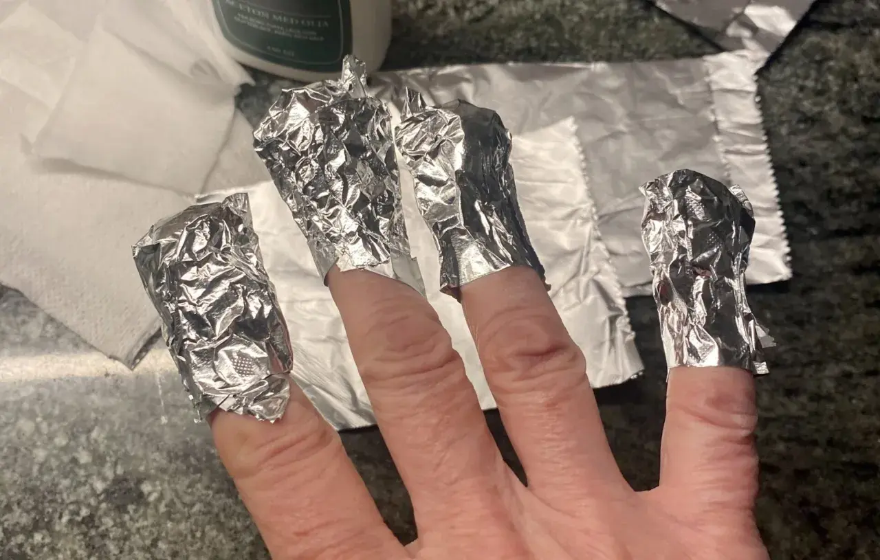 Fingrar inslagna i folie för att ta bort gellack hemma.