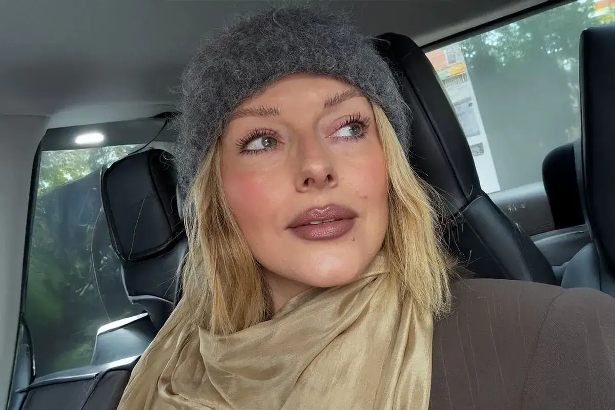 En kvinna i bil med en grå mössa och en beige scarf. Hennes smink rutin ger henne en fräsch look.
