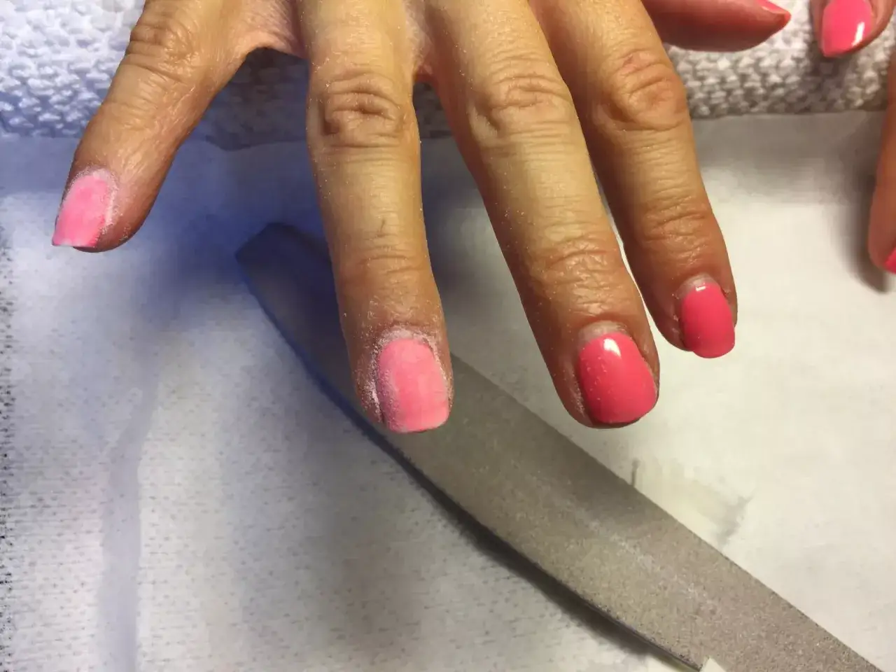 En hand filar bort rosa gellack. En nagelfil ligger bredvid.