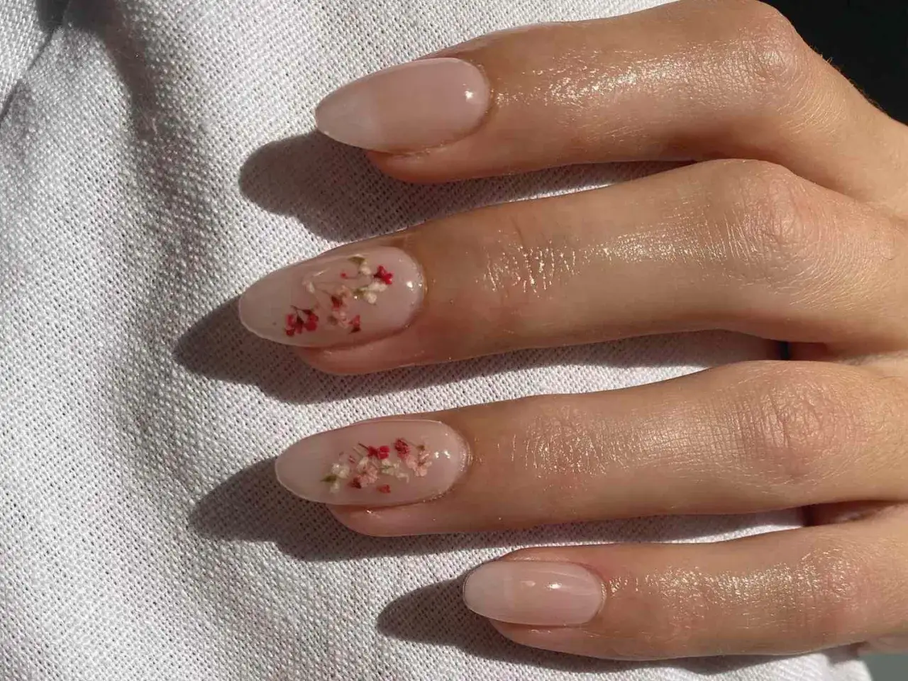 Vackra naglar med blommor i en naturlig, ljusrosa nyans. Små, torkade blommor är inbäddade i nagellacket för en unik och delikat look.