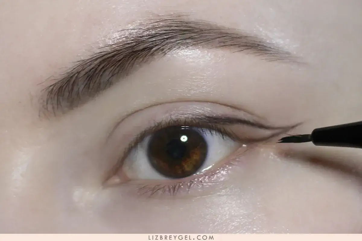 Närbild på ett öga där någon håller på att måla eyeliner. En svart eyelinerpenna drar en skarp linje längs ögonlocket.
