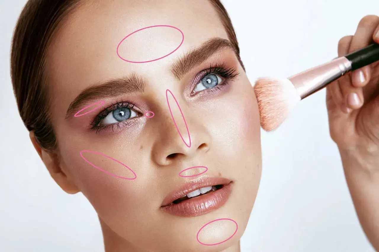 En makeupartist visar var man ska applicera highlighter för att framhäva ansiktets drag.