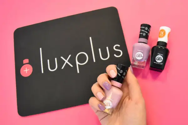 Få till perfekt shellac hemma med Sally Hansens gel-lack. En hand med målade naglar håller en ljusrosa flaska, bredvid två andra flaskor och en Luxplus-logga.