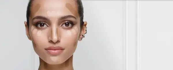 En kvinna förbereder sig för att applicera concealer. Hon har ljusa och mörka nyanser av smink på kinderna, näsan och pannan för att forma ansiktet.