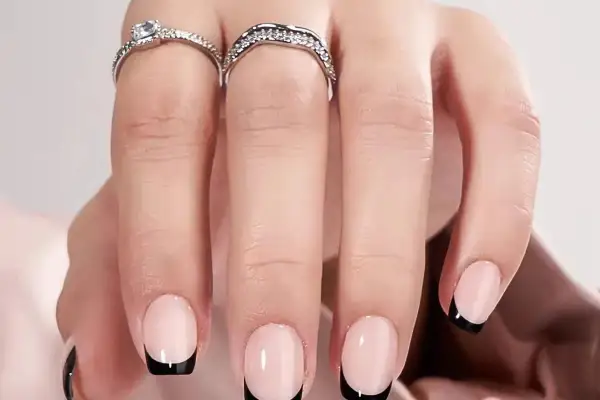Ett par händer med eleganta press on nails i fransk manikyr med svarta toppar. Två glittrande ringar pryder fingrarna.