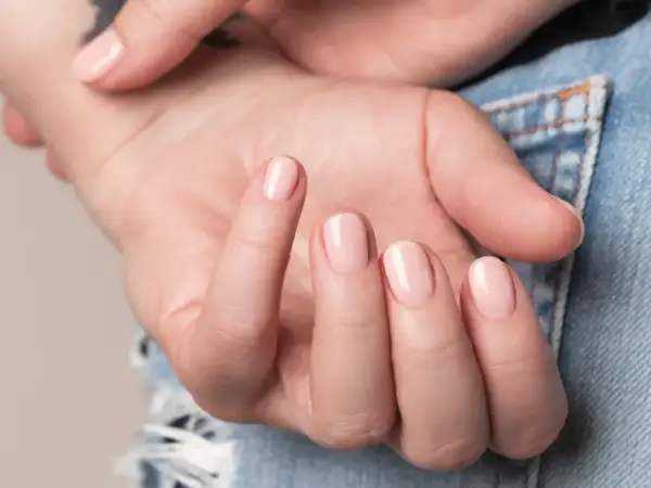 Nära bild på en hand med ljusrosa, glansiga naglar som ser ut som lipgloss nails.